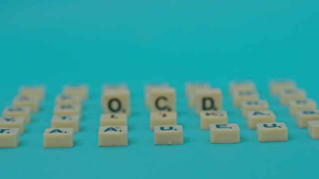 Rack Focus Shot Revealing "Ocd" Spelled Out With Letter Tiles Among Grid Of Random Characters On Turquoise Background