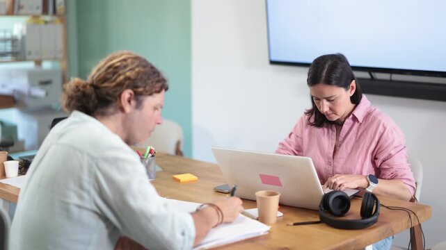  Adult male and female colleagues working with laptop and taking notes on paper documents in office
