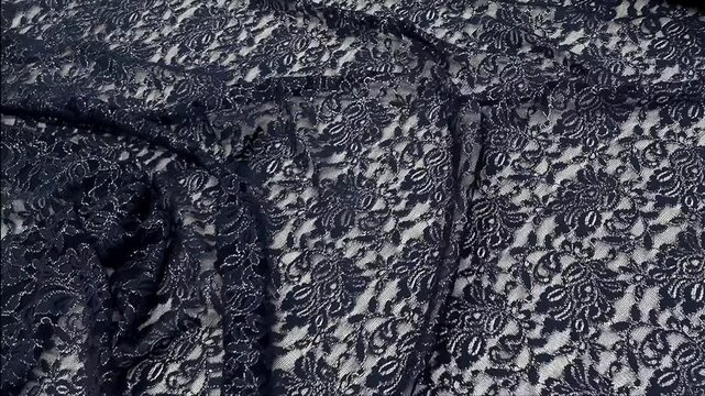 A sheer navy blue lace material features intricate floral motifs accented by shimmering silver glitter highlights providing a sophisticated texture for evening wear and formal garments