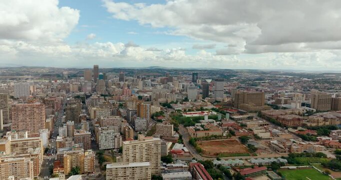 4K aerial zoom in shot over Johannesburg city center. High-angle drone footage showing dense urban architecture, skyscrapers, and street layouts of South African metropolitan neighborhood.