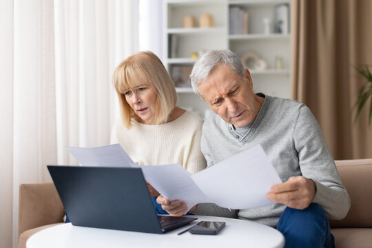 Concerned senior couple reading financial papers at home, looking worried about bills, stressed elderly spouses doing expenses or retirement budget management