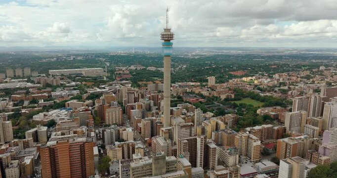 Epic 4K drone zoom out from Hillbrow Tower. Dramatic establishing shot revealing the vast Johannesburg skyline, dense urban architecture, and metropolitan horizon across the South African landscape