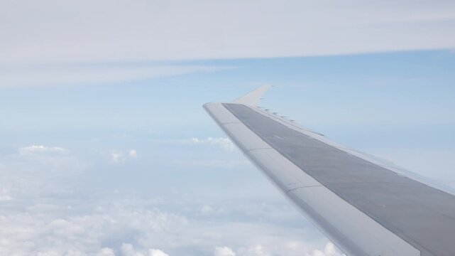 view through aircraft window with plane's wing over blue sky with white fluffy clouds from airplane flight fly over the clouds in a sunny day with cloud moving,summer travel vacation background