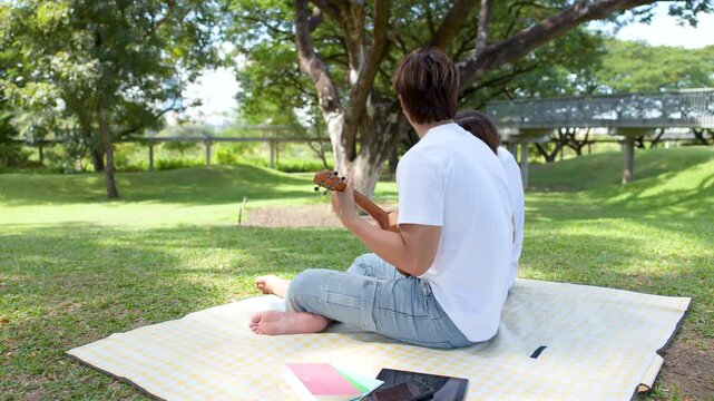 Young Asian Couple Having a Picnic and Playing Ukulele in Park