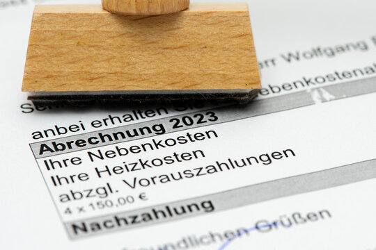 Ein Holzstempel mit Freiraum f&uuml;r individuellen Text steht auf einer Nebenkostenabrechnung f&uuml;r eine Mietwohnung mit Berechnung des pers&ouml;nlichen Verbrauchs und einer Nachzahlung. - Symbolbild