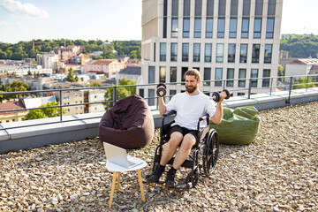Obraz premium A man with a beard in a wheelchair is exercising with dumbbells on a rooftop terrace with a city view