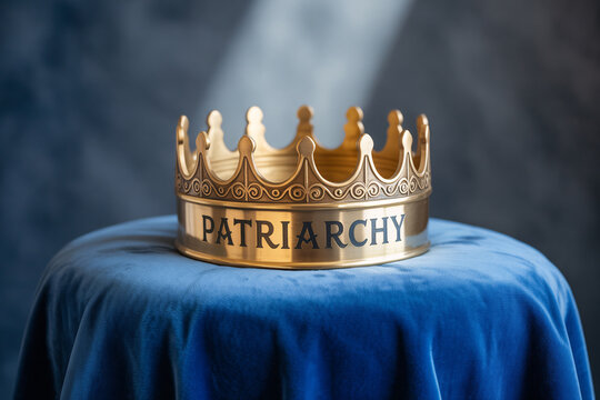 Golden crown with the word "Patriarchy" resting on blue fabric. Symbol of power and societal patriarchy