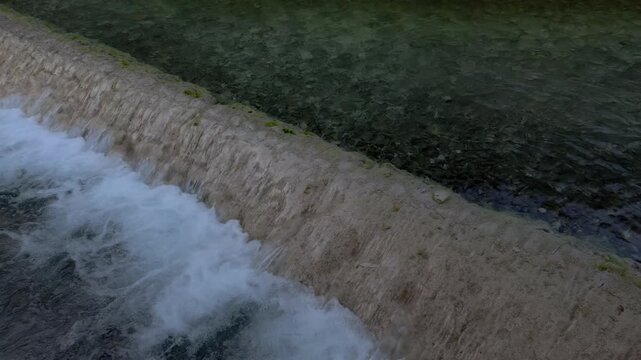 Slow motion closeup of foamy water falling over weir