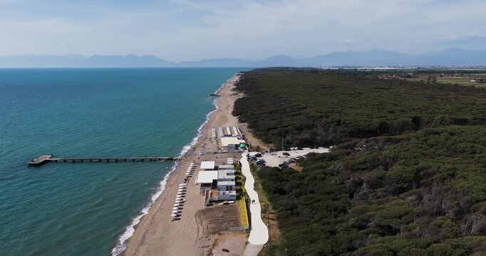 Aerial view of the sandy beach with a long pier and a lush pine forest bordering the turquoise sea in Capaccio, Campania, Italy.