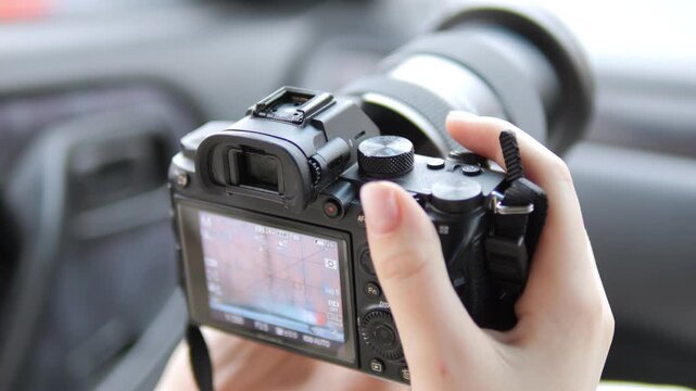 Hand holds camera inside car. View shows rear screen and lens. Focus shifts slightly across frames. Car interior blurred in background. Neutral lighting on equipment. No animals or plants visible