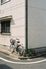 Fototapeta premium Classic blue city bicycle with front basket parked at white building corner for urban lifestyle and Japanese street aesthetic