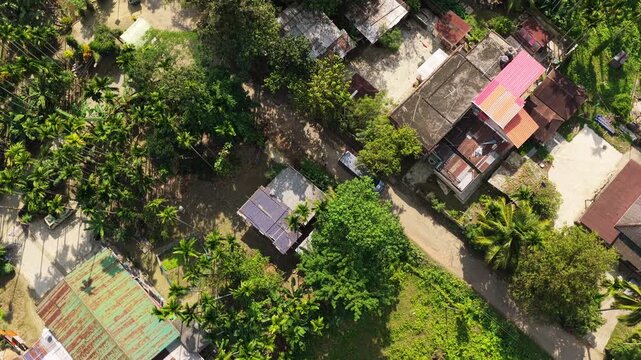 Birds eye view of a small van driving through a rural Indian village surrounded by dense tropical trees and traditional houses.