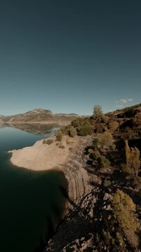 Cinematic vertical FPV drone shot flying over a scenic mountain reservoir with crystal clear reflections and autumn foliage. Captures the natural beauty of Leon, Spain for social media.