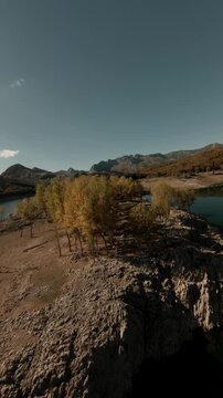 A vertical cinematic FPV drone sequence flying over rocky ridges and autumn trees at the Porma Reservoir in Leon, Spain. Ideal for travel social media and nature documentaries.