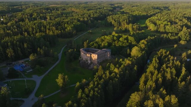 Aerial tilt away shot of Raasepori castle ruins surrounded by dense sunset forest