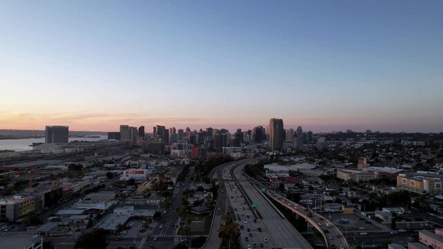 Drone pulling back above the freeway at sunset revealing a wide shot of the downtown San Diego skyline and surrounding city.