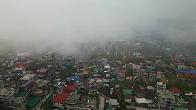Aerial flyover of Quirino Hill in Baguio, Philippines with dense urban neighborhood, mountain terrain, and low clouds covering the cityscape
