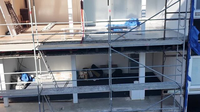 Exterior view of a building undergoing renovation with scaffolding and construction materials. Scaffolding surrounds a multi-story building in the process of renovation, revealing interior spaces and