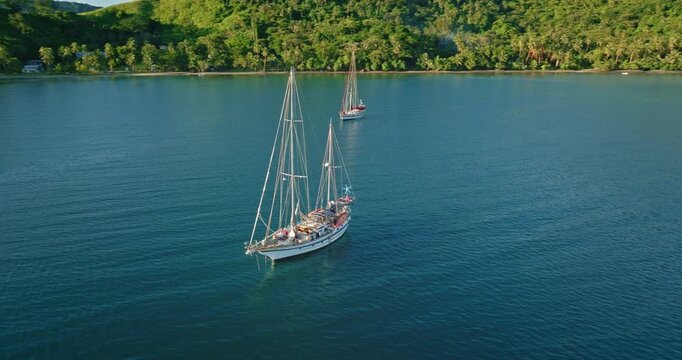 Sailboats anchoring in a serene tropical bay, tranquil ocean scene with lush green islands and clear blue water, representing travel, adventure, and idyllic island life Aerial drone cinematic video