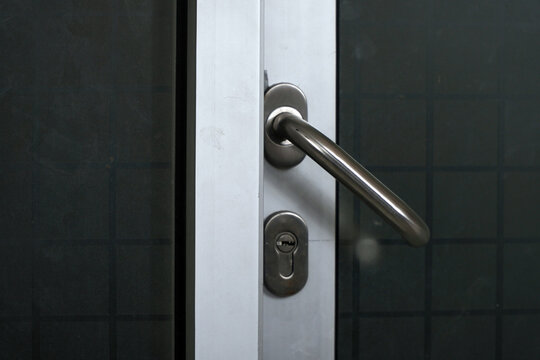Close-up of a modern metallic door handle and keyhole lock on a silver aluminum frame. Minimalist glass door design for office or residential building, focusing on security and interior hardware detai