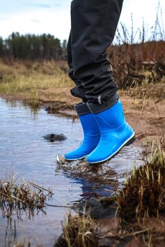 Child jumping in water with blue rubber boots splashing outdoors