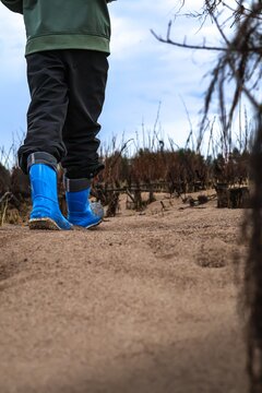 Child walking on sandy ground in blue rubber boots in natural environment