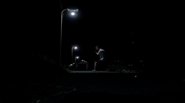 Cinematic 4K ground view of a man training Muay Thai shadowboxing under a street lamp in a dark, mysterious alley. Moody urban atmosphere and gritty fight practice.