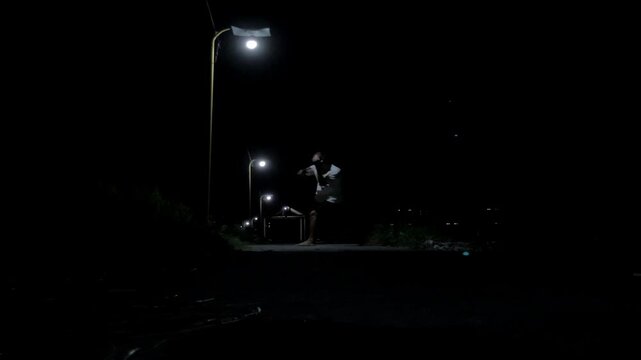 Cinematic 4K ground view of a man training Muay Thai shadowboxing under a street lamp in a dark, mysterious alley. Moody urban atmosphere and gritty fight practice.