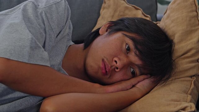 Depressed young adult lying down looking toward camera with somber and worried look on sofa