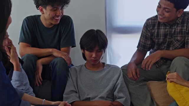 Quiet male adult looking down with sad expression as peers socialize during gathering on sofa