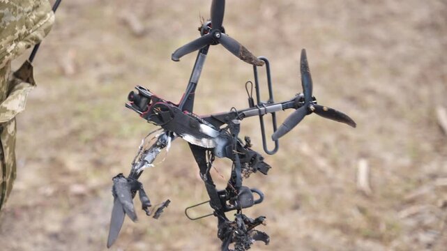 Person holding burnt FPV drone frame with visible damage and exposed components outdoors