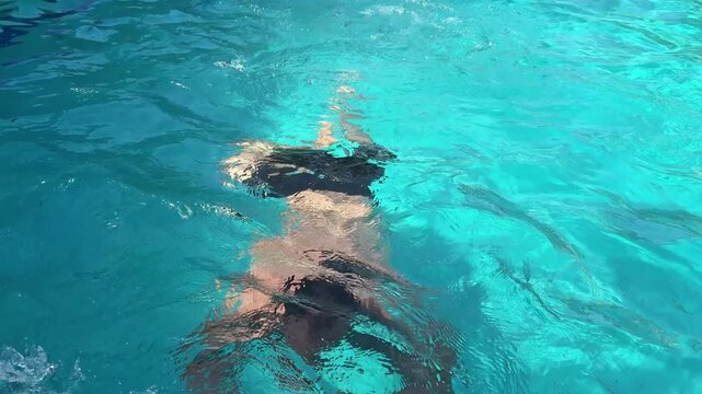person diving underwater in clear swimming pool during sunny summer vacation recreation activity