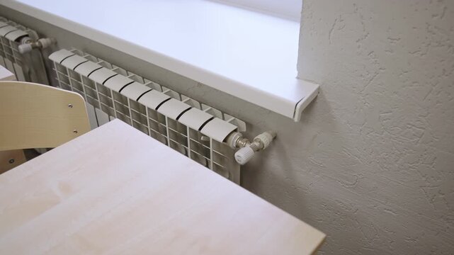 Contemporary heating unit stands against textured wall below window ledge near wooden desk. View suggests comfortable indoor temperature