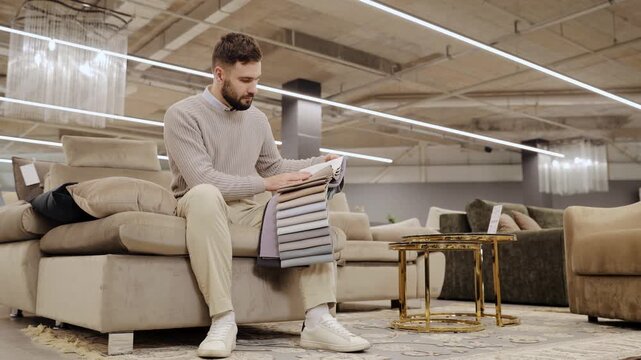 Man holding textile swatches, comparing different fabric options for new sofa in a furniture store, making a selection