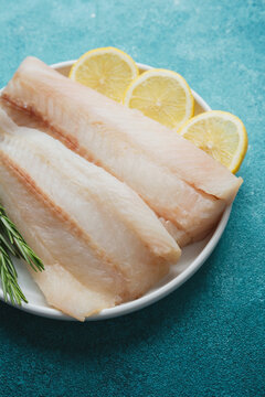 Raw pollock fillet with lemon slices and rosemary on blue background