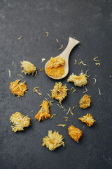 Obraz premium Dried chrysanthemums scattered on dark textured surface with wooden spoon