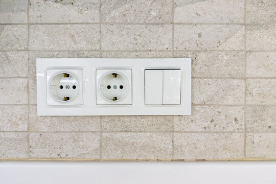 White power outlets and light switches on a textured tiled wall