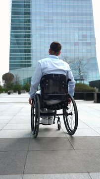 Back view of a young professional with a disability using a wheelchair in a modern business district. He moves forward with determination