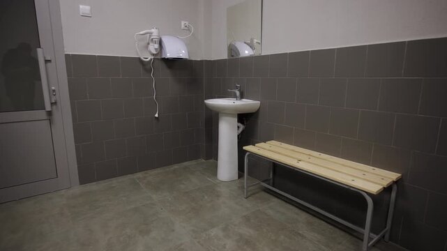 Public restroom wash area features minimalist pedestal sink and wooden bench. Functional design looks simple. Dark interior concept