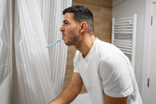 A man focused on his morning oral hygiene routine, brushing his teeth while looking into the bathroom mirror.