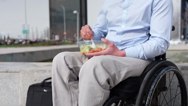 Businessman with a physical disability eating a healthy lunch from a takeaway container. Concept of inclusion and accessibility in the workplace