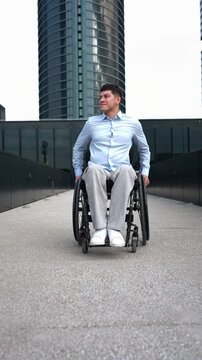 Confident young businessman with a physical disability moving forward in his wheelchair through a modern city with skyscrapers in the background