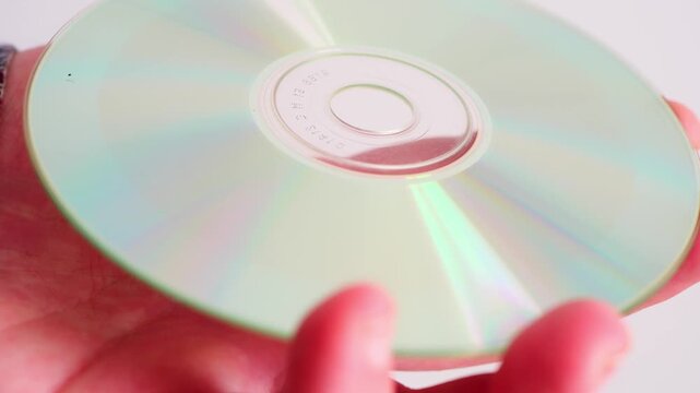 close-up of hand holding a compact disc, reflective surface showing rainbow light and metallic texture. Ideal for technology concepts, data storage themes and retro media visuals