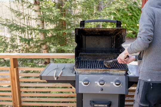 Cleaning outdoor barbecue grill with wire brush on wooden terrace in summer cottage backyard