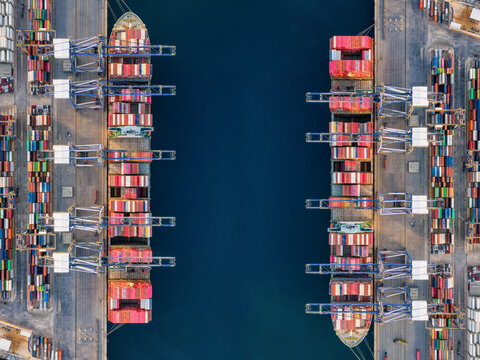 High aerial overhead view of a large container cargo ship terminal with two super cargo ships docked and unloading activity