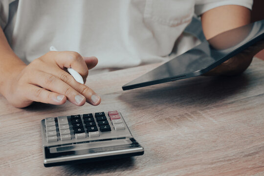 Hand Using Calculator and Holding Tablet on Wooden Desk, Financial Accounting and Business Technology Concept