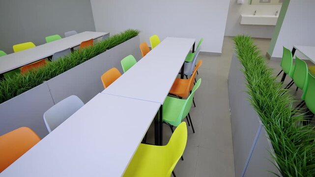 Brightly colored ergonomic chairs alternate along white tables.High angle shot captures perfect symmetry of canteen dining furniture
