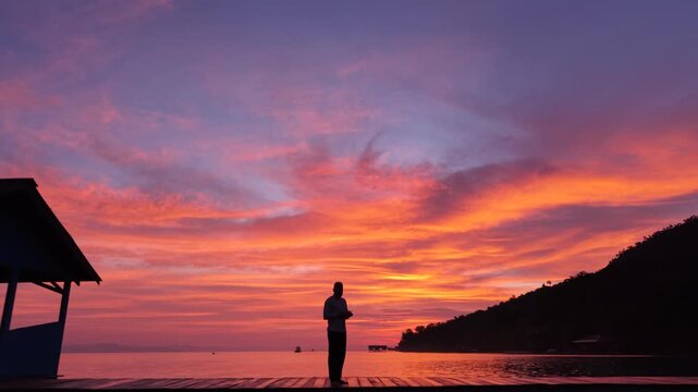 Drone Aerial View of Silhouetted People on Tropical Pier During Colorful Sunset in Raja Ampat Indonesia