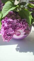 Obraz premium A bouquet of blooming lilacs with green leaves in a round glass vase