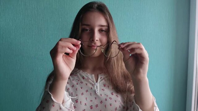 Teen girl inspecting eyeglasses lens indoors, vision care routine, personal maintenance and lifestyle concept.